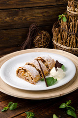 Apple strudel with creamy ice cream, garnished with mint on a white plate on a short wooden background