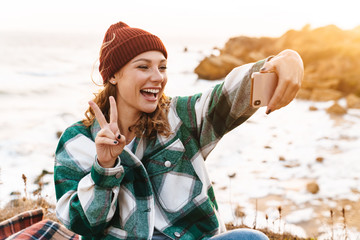 Image of woman taking selfie on smartphone and gesturing peace sign