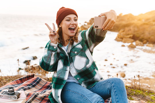 Image of woman taking selfie on smartphone and gesturing peace sign