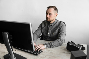 Young businessman or student in a shirt sitting against monitor of computer. Working on a pc at a table in the office with a thoughtful expression. Young businessman working on his laptop in office.