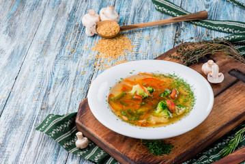 Vegetable broth, soup with broccoli, asparagus, carrots, onions, bell peppers and greens in white plate