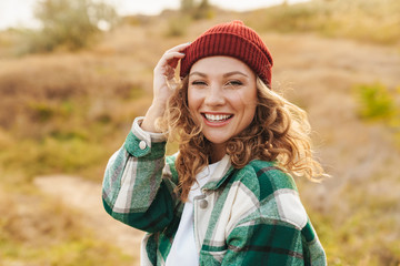 Image of young woman wearing hat and plaid shirt walking outdoors