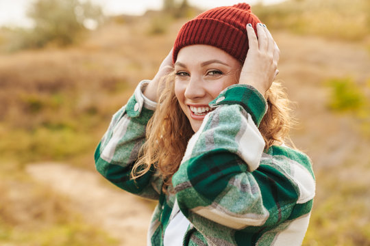 Image of young woman wearing hat and plaid shirt walking outdoors