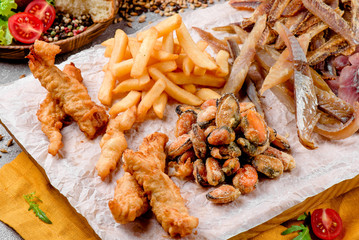 Assorted beer snacks: fried mussels, dried fish, french fries, cheese sticks on kraft paper on tray