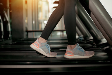 Lower body at legs part of Fitness woman running on running machine or treadmill in fitness gym with sun ray. Warm tone. Healthy and Exercise activity concept. Workout and Strength training theme.