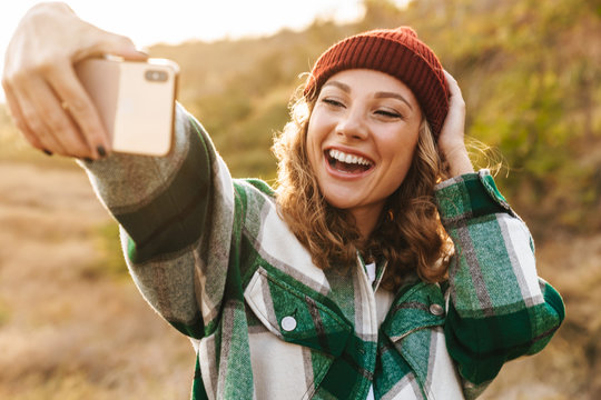 Image of woman taking selfie photo on cellphone while walking outdoors
