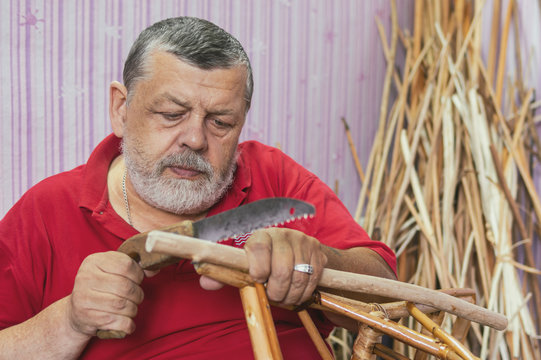 Portrait of Caucasian senior craftsman making kids wicker chair from withe
