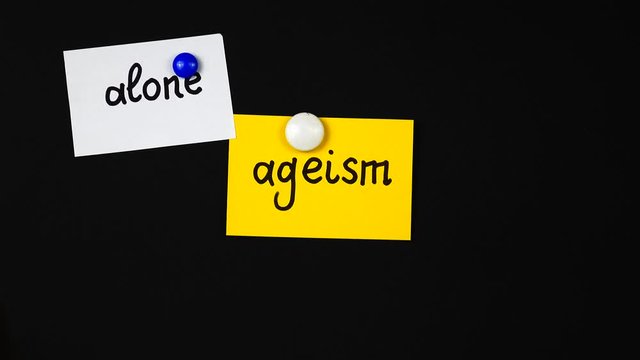 Lecturer places on magnetic board sheets of paper with the terms related to ageism at a lecture on the problem of ageism. Using of a visual aids