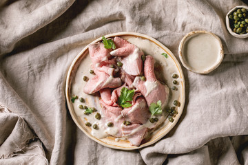 Vitello tonnato italian dish. Thin sliced veal with tuna sauce, capers and coriander served on ceramic plate over grey linen cloth as background. Top view, copy space - obrazy, fototapety, plakaty