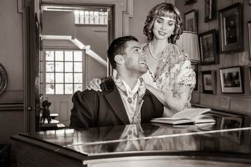 Vintage couple in period costume sitting around piano playing tunes and singing songs