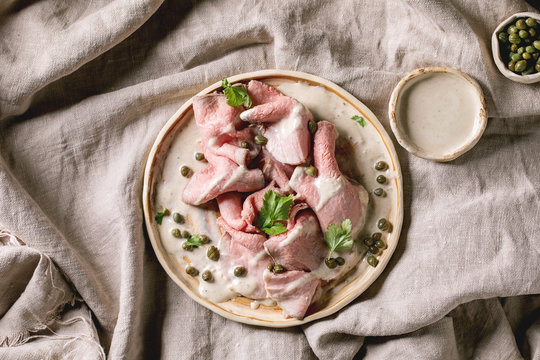 Vitello tonnato italian dish. Thin sliced veal with tuna sauce, capers and coriander served on ceramic plate over grey linen cloth as background. Top view, copy space