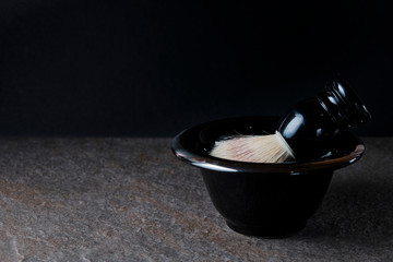 Shaving brush and bowl on the stone surface at black background
