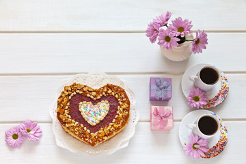 Homemade heart-shaped cake, two cups of coffee, gifts in boxes and a bouquet of flowers on white table. Beautiful congratulations on Valentine's Day or Happy Birthday. Flat lay, copy space, top view