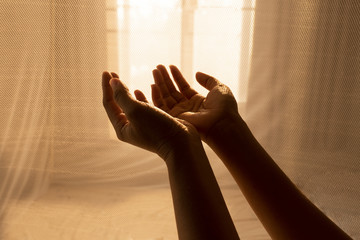 hands of woman pray for religion service with sunlight trough light curtain background