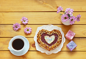 A beautiful congratulation on Valentine's Day or Happy Birthday: fresh homemade heart-shaped cake and a bouquet of flowers on wooden table. Festive background, flat lay, copy space, top view, close-up