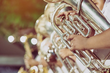 Male student with friends blow the euphonium with the band for performance on stage at night.