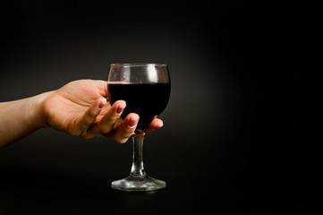.female hand with a glass of wine on a dark background