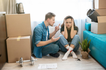Fototapeta na wymiar couple man and woman have conflict sitting on the floor during unpacking boxes, woman closes her ears, man cries , moving process
