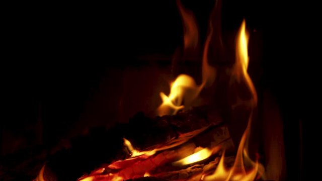 Close up of wood burning into fireplace, looping video of fire flames playing around red orange burned wood on black background