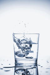 Clear mineral water splashes in a glass with ice.