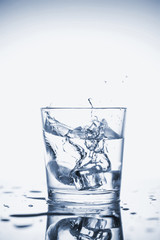 Clear mineral water splashes in a glass with ice.
