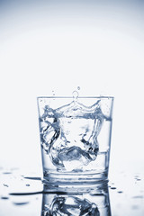 Clear mineral water splashes in a glass with ice.