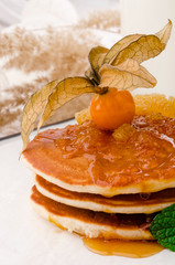 Beautiful pancakes with physalis jam, decorated with physalis berry on a white plate on a light spring background