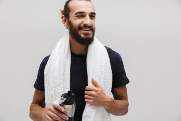 Image of sportsman with towel over his neck drinking water after workout