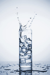 Clear mineral water splashes in a glass with ice.