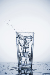 Clear mineral water splashes in a glass with ice.