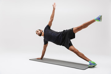 Image of attractive sportsman in tracksuit doing workout on yoga mat
