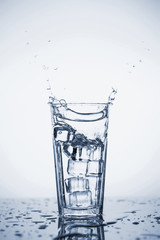 Clear mineral water splashes in a glass with ice.