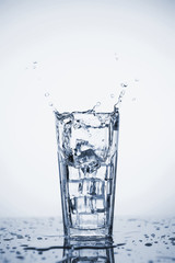 Clear mineral water splashes in a glass with ice.