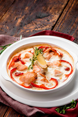 Baked salmon in a creamy sauce with tomatoes in a white plate on a dark wooden background with a burgundy napkin. Close-up. Space. Top view. Series of Photo