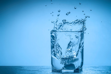 Splash of water in a glass cup on a blue background with place for your text.