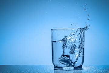 Splash of water in a glass cup on a blue background with place for your text.