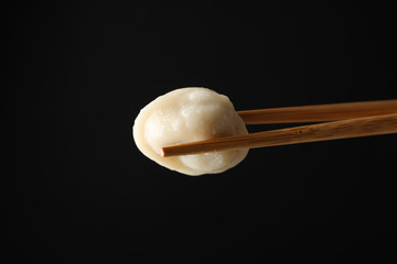 Chopsticks with dumpling on black background, close up