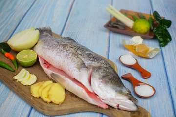 Wooden cutting board   with baramundi, salt, msg,ginger,garlic,onion,key lime, chilies,  and lemongrass over the wooden background.