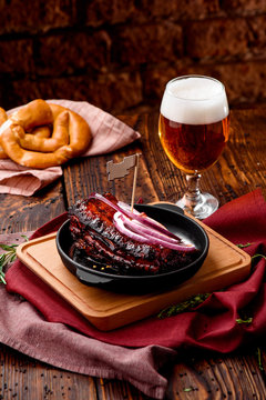 Popular Beer Snack. Pork Ribs In Barbecue Marinade With Honey In Cast-iron Pan On Wooden Board And Glass Of Beer