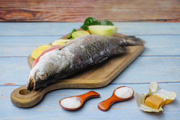 Wooden cutting board   with baramundi, salt, msg,ginger,garlic,onion,key lime, chilies,  and lemongrass over the wooden background.