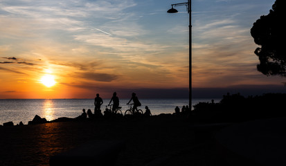 Fototapeta na wymiar Dramatic and beautiful sunset at the coast line of the mediterranean sea in trieste Italy with silhouettes of a couple and people sitting on the beach.