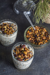 Healthy and healthy breakfast, granola with nuts in the mugs drenched in yogurt and a bowl with dry granola on a background of a dark table and plants