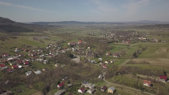 Cieklin, Poland - 7 7 2019: Roman Catholic Church in the center of a picturesque village located on green hills. Aerial drone or quadrocopter aerial view. European farms. Private Farm Panorama