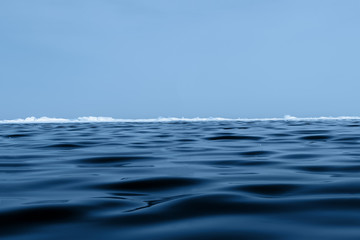Fototapeta na wymiar Background texture of blue wavy ice of Lake Baikal with hummocks on the horizon and blue sky