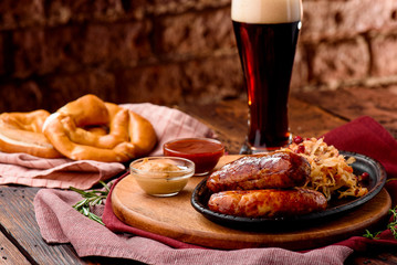 Glass of dark beer with foam and fried sausages with cranberry-honey stewed cabbage served in cast-iron pan