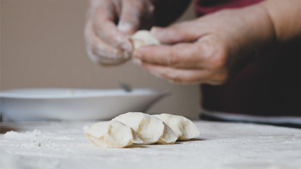 Mature female hands making dumplings with cheese at home kitchen, close-up.