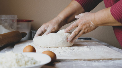 Close-up hands of senior female is kneading a dough in flour on the table at home kitchen, side view