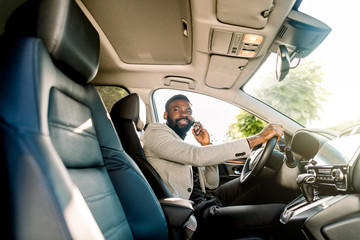 Young African American man in smart casual business wear, using phone sitting in the car, side view