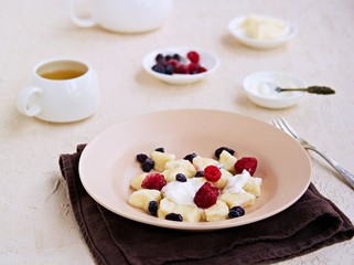 Lazy dumplings or gnocchi from cottage cheese in a clay plate on a light concrete background. Served with sour cream, berries. Dishes from cottage cheese. Useful breakfasts. Selective focus.