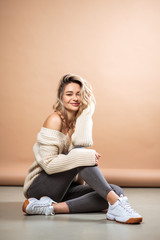 Beautiful blonde woman in a knitted sweater over brown background. Casual style, fashion beauty portrait